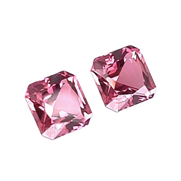 157_2 - GEMWORLD LTD Three pink faceted gemstones scattered on a white background and catching light at the edges