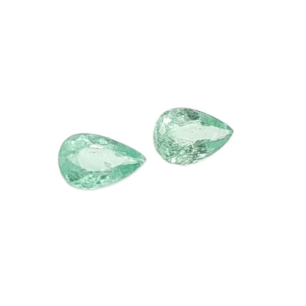 Several green, rough gemstones scattered on a white background, resembling emeralds/berries in shape and color.