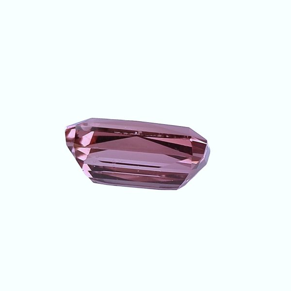 Tour 129_3 - GEMWORLD LTD Close-up of a faceted pink gemstone against a pale background, showing its angular cuts and reflective facets.
