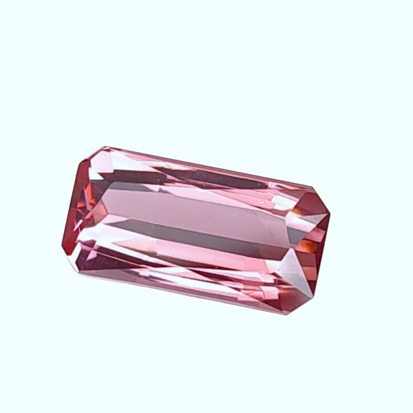 Tour 134_6 - GEMWORLD LTD Close-up of a faceted pink gemstone against a pale blue background.