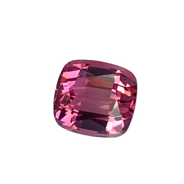 Tour 2_1 - GEMWORLD LTD Close-up of a faceted pink-red gemstone with multiple angular facets in a rounded oval shape, resembling a ruby jewel